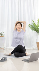Beautiful Asian woman in sportswear is warming up or doing light exercises in the house with dumbbells and a protein shake or bottle of water and using a laptop at home, Healthy exercise.