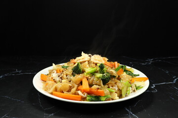 Fried rice noodle mixed with Chinese kale, carrot, broccoli, peeled shrimp and squid serving on the plate. Famous seafood menu in Asia restaurant. 
