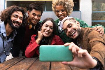 Obraz premium Smiling multiracial young friends take selfie together with mobile phone outdoors