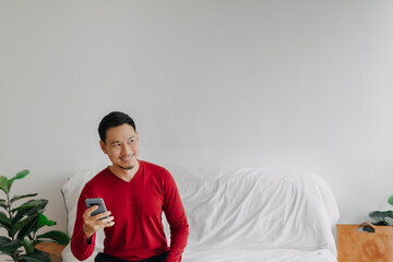 Happy asian man on sofa use phone for trading business with advertising space. 