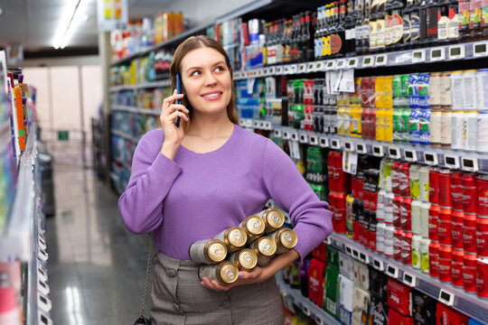 Young female with cans of beer in her hands consults on a mobile phone.