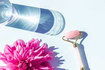 Beautiful pink flower and crystal rose quartz facial roller on blue background. Facial anti-age massage. Concept youth, beauty and self-care
