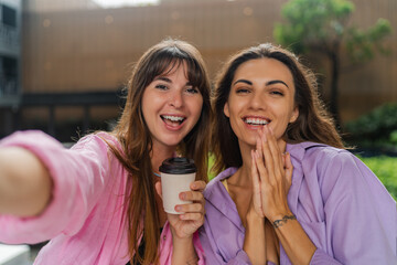 Close up self portrait of two happy women enjoing shopping, drinking coffee. Wearing colrful casual...