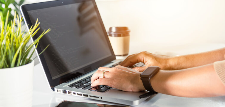 Web application development. programmer woman writing program code sitting at workplace in office, software developer hands coding HTML programming with laptop computer, IT start up concept, back view