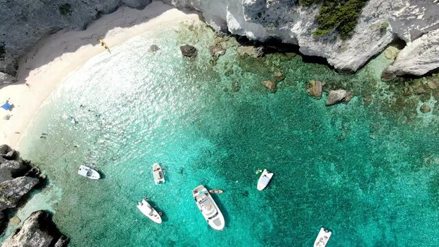 A drone flies above Tremiti Island in Italy, zooming in on a yacht and other vessels cruising in the island's azure waters as people swim nearby.
