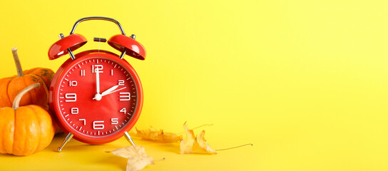 Alarm clock and autumn leaves with pumpkins on yellow background with space for text