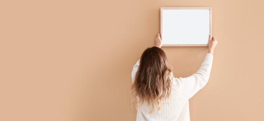 Woman hanging blank photo frame on beige background with space for text