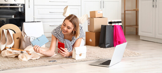 Young woman with mobile phone, laptop and new purchases in kitchen. Online shopping concept