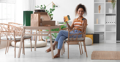 Young African-American woman with credit card and many shopping bags at home