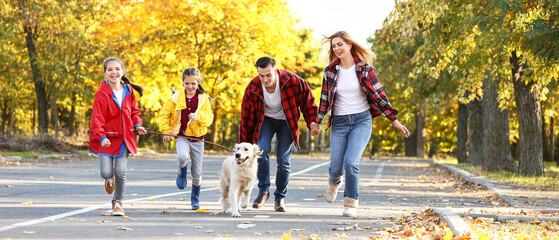 Happy family with dog running in autumn park