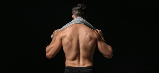Sporty muscled man with towel on dark background, back view