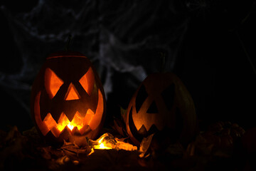 Halloween's holiday attributes. Lantern carved from pumpkin known as Jack-o-lantern glow in the dark on a black background with spider webs, autumn leaves and balloons. Trick or treat