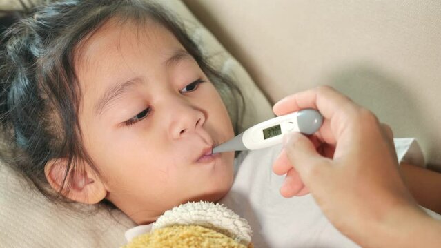 Sick kid. Mother parent checking temperature of her sick daughter with digital thermometer in mouth, child laying in bed taking measuring her temperature for fever and illness, healthcare