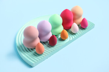 Stand with colorful makeup sponges on blue background