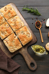 Board with tasty Italian focaccia, oil and peppercorns on dark wooden background