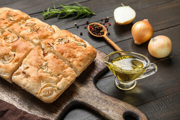Board with tasty Italian focaccia and gravy boat of oil on dark wooden background, closeup