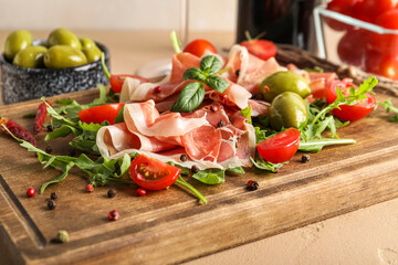 Wooden board with delicious jamon, greens and tomatoes on table, closeup