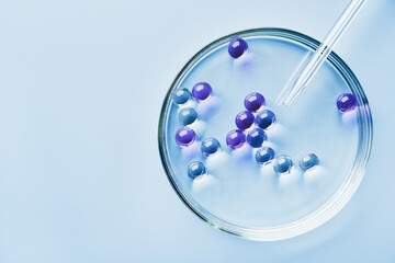 Lab dropper with sample of gel bubbles in petri dish on blue background, hard shadows. Abstract...