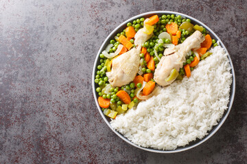 Chicken drumsticks stewed with carrots and green peas, served with rice close-up in a plate on the table. Horizontal top view from above