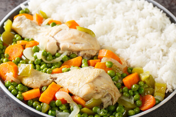 Chicken drumsticks stewed with carrots and green peas, served with rice close-up in a plate on the table. Horizontal