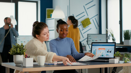 Startup employee working with african american coworker on group project comparing sales charts on...