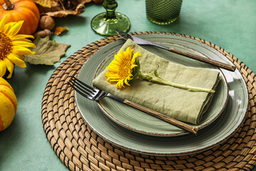 Stylish dinnerware, sunflower and autumn decor on green table
