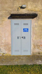 Wall with an electrical substation. White writing in Italian: ELECTRIC CABIN on the blue background. Vertical image.