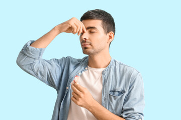 Young man with nosebleed and tissue on blue background