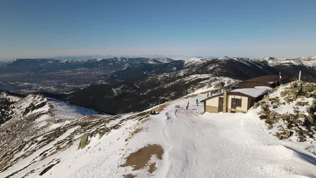 Pull back shot from a ski station with skiing people arriving. Revealing an endless mountain range in the background.