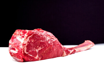 Obraz premium Fresh uncooked tomahawk steak on the bone on white cooking paper and black background. Prime cut of beef. High quality product with marbling and delicate flavor for special occasion. Butcher craft.