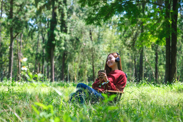 Naklejka na ściany i meble Portrait of a young woman enjoy listening to music with headphone and drinking coffee while sitting on a camping chair in the park