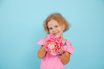 Charming little girl show beautiful floral craft on empty blue background, free copy space. Blue eyed child of kindergarten age hold paper pink flower. Children creativity and fantasy