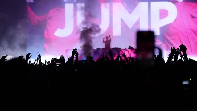 Silhouette of DJ hyping concert fans to jump with flashing big screen cryogenics