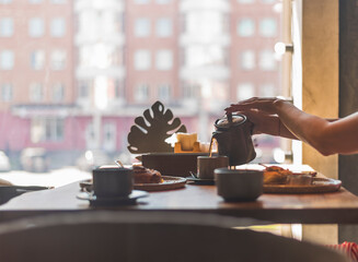 a girl pours tea from a teapot into a cup at a table in a cafe,