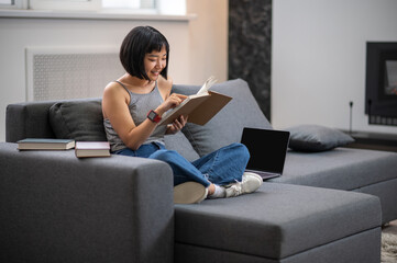 A short-haired young woman reading a book while sitting on the sofa