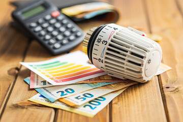 Thermostatic valve head, euro money and energy label on wooden table. Concept of increasing heating prices. © Jiri Hera