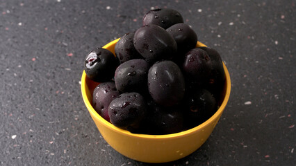 Jambul or Jamun (Syzygium cumini) in yellow bowl isolated on textured background.