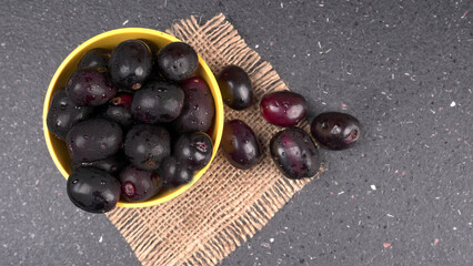 Jambul or Jamun (Syzygium cumini) in yellow bowl isolated on textured background.
