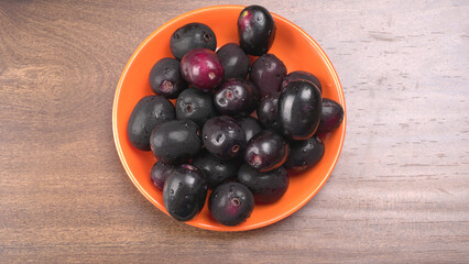 Jambul or Jamun (Syzygium cumini) in yellow bowl isolated on textured background.