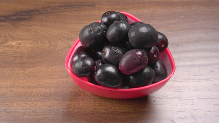 Jambul or Jamun (Syzygium cumini) in yellow bowl isolated on textured background.