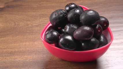Jambul or Jamun (Syzygium cumini) in yellow bowl isolated on textured background.