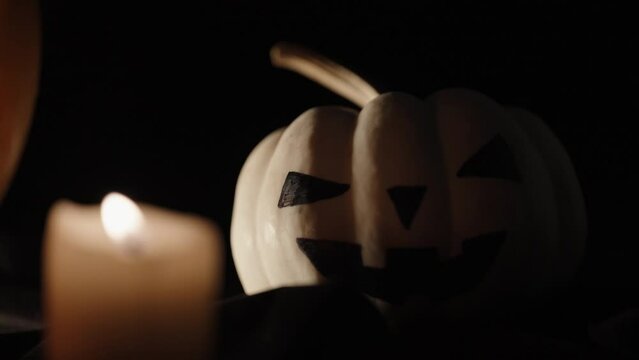 A white pumpkin for Halloween, and a candle. Black background close-up.