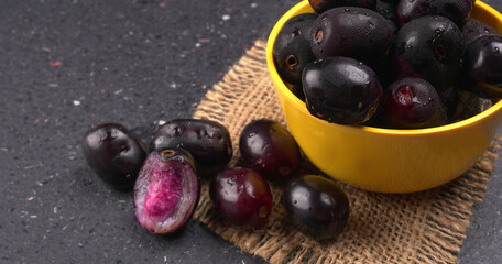 Jambul or Jamun (Syzygium cumini) in yellow bowl isolated on textured background.