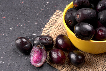 Jambul or Jamun (Syzygium cumini) in yellow bowl isolated on textured background.