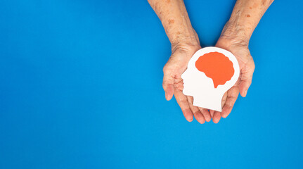 Top view of head with a brain made from paper on the palm senior woman over a blue background