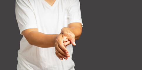 Close-up of a young man suffering from hand pain while standing on a gray background
