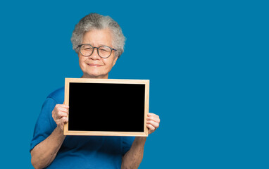 Senior woman holding a mini blackboard and looking at the camera with a smile while standing on a blue background