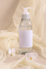 One pump refillable bottle near orchid flowers and tulle on light beige. Cosmetic packaging Mockup
