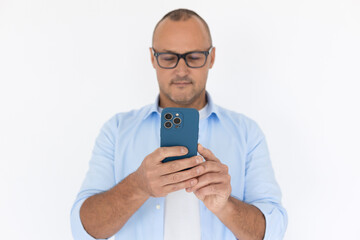 Portrait of confident mature man wearing glasses using phone. Balding Caucasian businessman wearing white T-shirt and blue shirt texting message on smartphone. Mobile communication concept