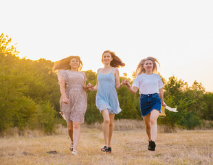Naklejka na ściany i meble A group of girlfriends jumps and runs outdoors. A group of female friends hugs and enjoys the sunset in nature. Laughter, smiles and joy.
